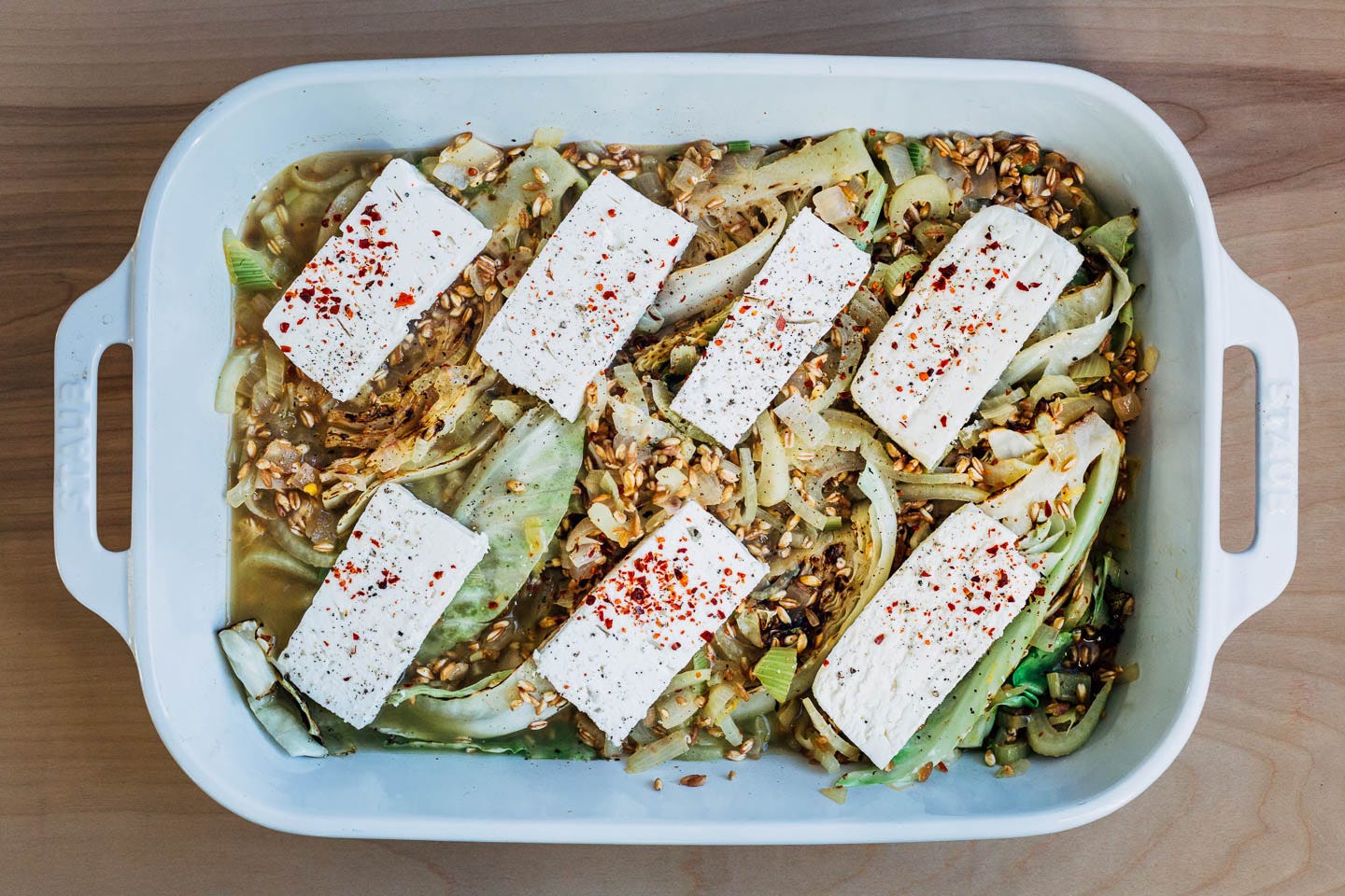 A baking dish with farro, cabbage and feta slices