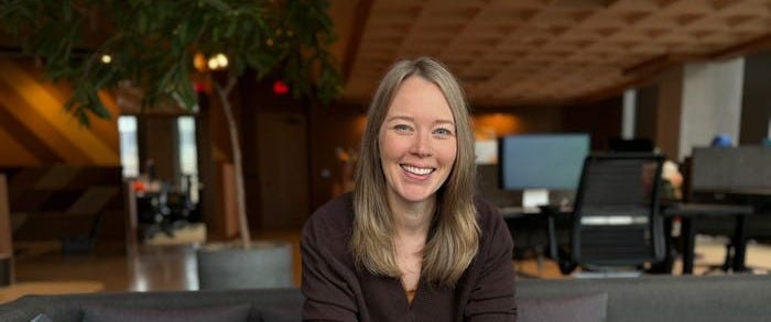 A woman sitting on a couch in an office and smiling at the camera.