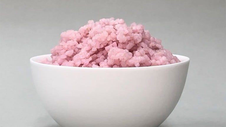 A white bowl of pink rice grains.