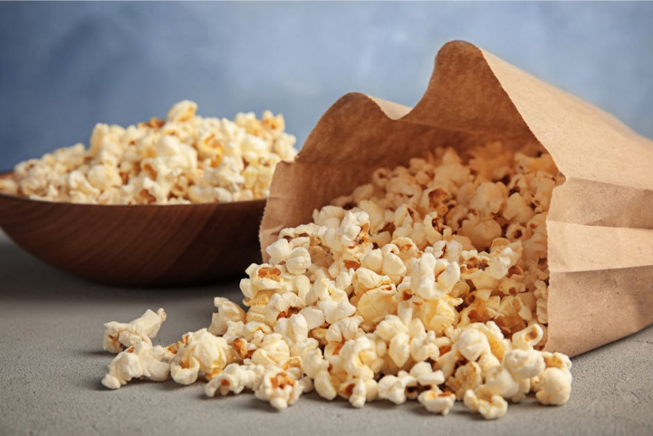 a brown paper bag of popcorn, spilling out, plus a large bowl of popcorn