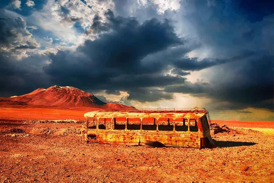 abandoned bus rusting in the desert under a story sky