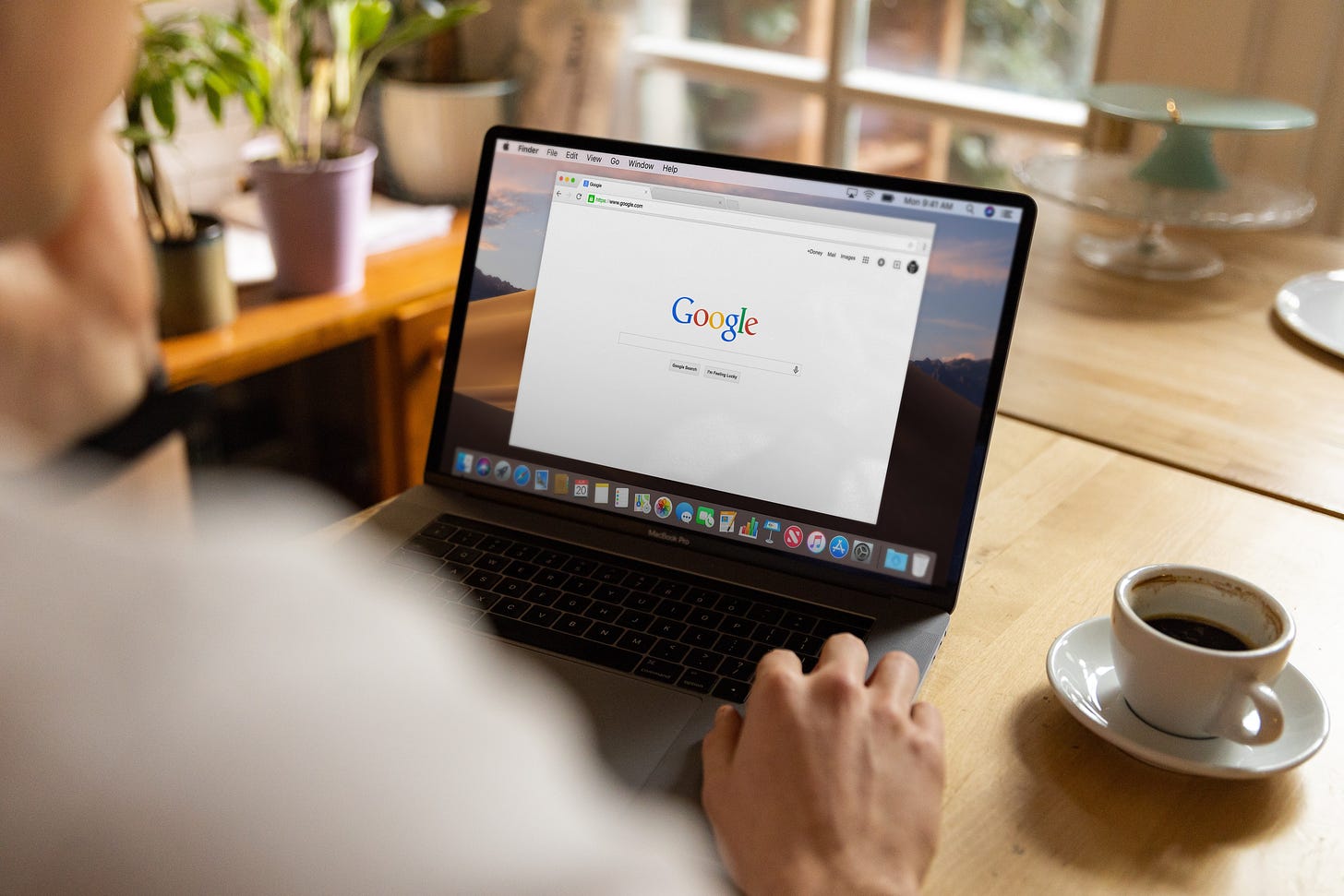 a man uses a laptop with the google search page open, a black coffee sits on the table beside him.