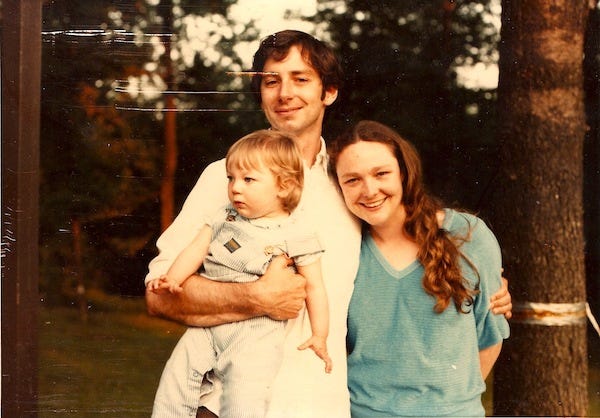 John, Betty and daughter J, about a year and a half old, smiling.