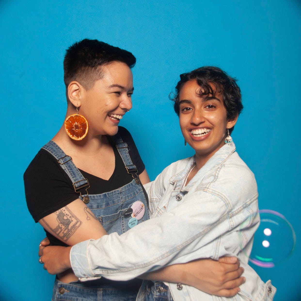 Ally and Anju embracing in front of a blue background