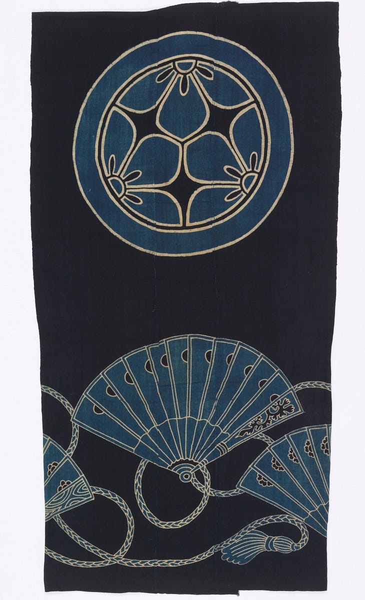A Japanese indigo-dyed textile, featuring patterns created with a stenciling technique. At the top, a large circular emblem, known as a mon, displays a stylized floral or geometric design. Below this, a dynamic arrangement of open and closed fans, intertwined with decorative cords and tassels, fills the lower portion of the fabric. A Japanese indigo-dyed textile, featuring patterns created with a stenciling technique. At the top, a large circular emblem, known as a mon, displays a stylized floral or geometric design. Below this, a dynamic arrangement of open and closed fans, intertwined with decorative cords and tassels, fills the lower portion of the fabric.