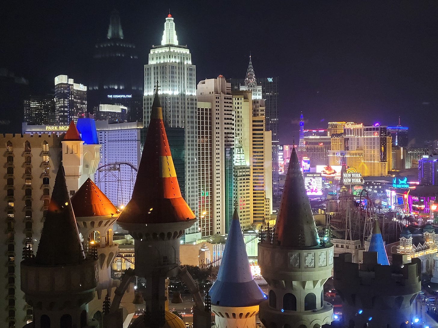 A view from a Vegas hotel room, with fairytale castle turrets in the foreground, New York in the background and the lights of the Strip in the distance