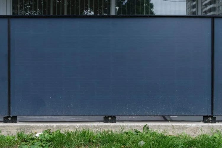 Large blue-grey solid panel containing solar panels and serving as an apartment balcony railing.