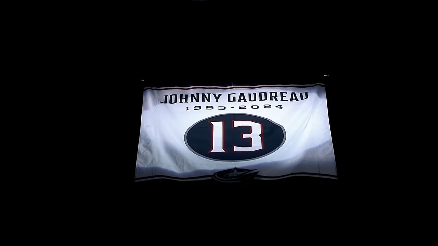 A banner hanging from the rafters in Nationwide Arena. It has a white background and on the top has the name "Johnny Gaudreau" and directly beneath it the years 1993-2024. In the middle is the number 13.