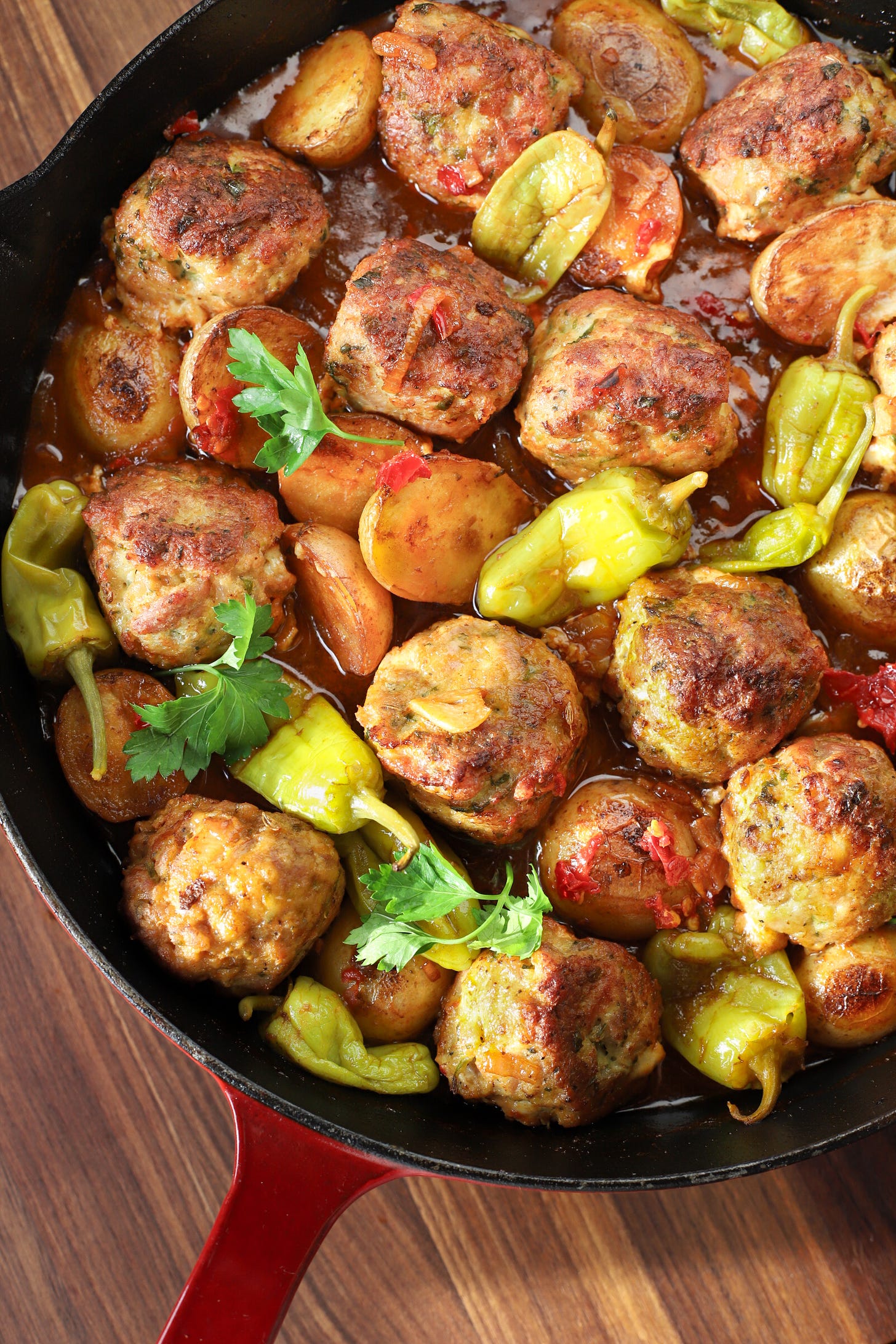 Skillet with meatballs, pepperoncini, and potatoes in a spicy sauce