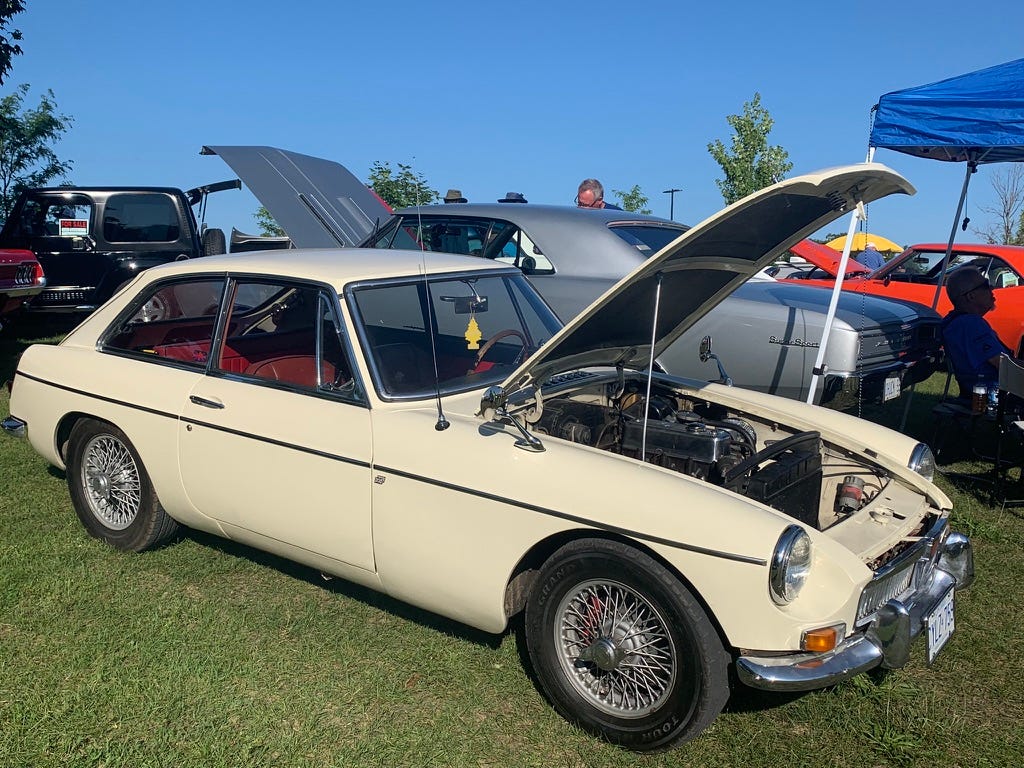 Steedan's car, a 1968 MGB GT in British White, with red leather interior. The hood is open and the car is parked at a car show