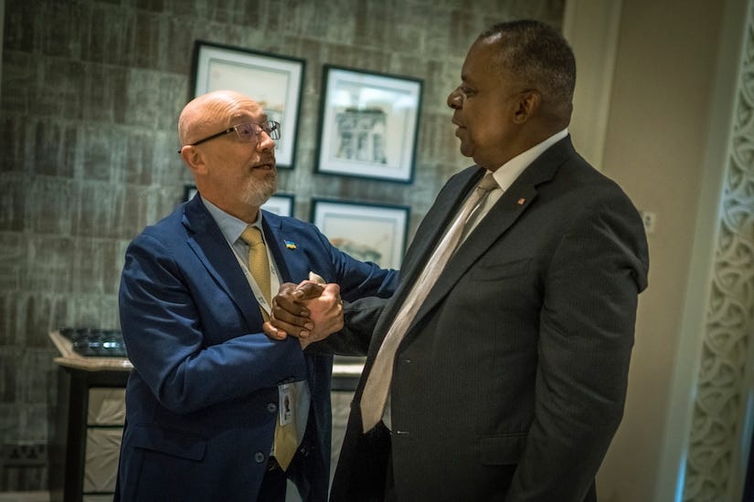 Two men wearing suits shake hands.