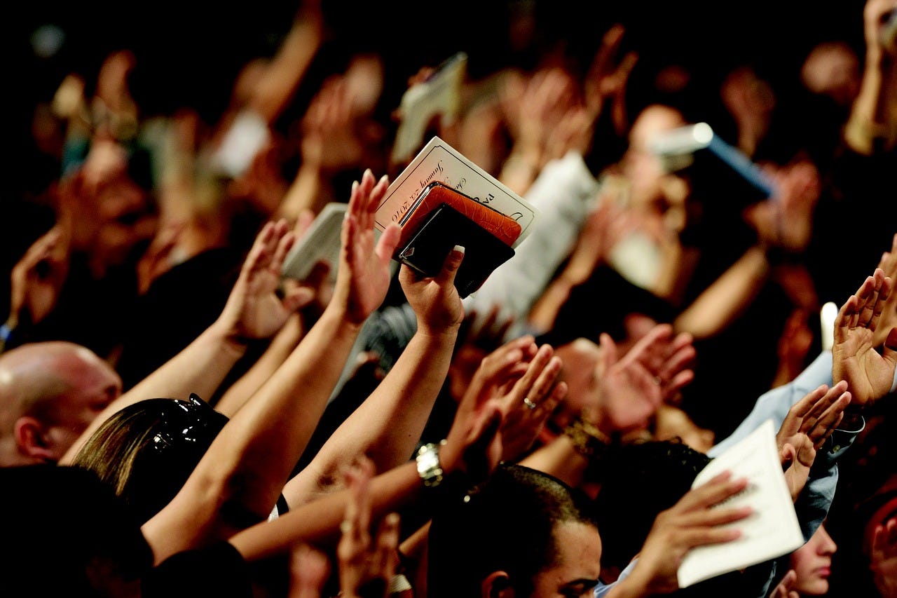 People with raised hands, one of them holding a Bible and an electronic tablet, at a Protestant church service
