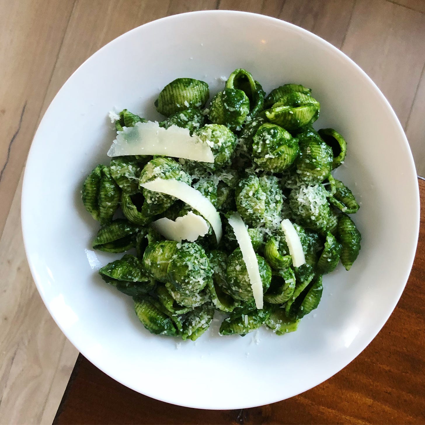 A bowl full of shell pasta covered in vibrant green kale sauce, strips of shaved parmesan, and grated parmesan.