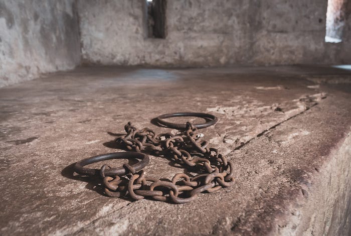 Photo of a concrete cell with chains and handcuffs.