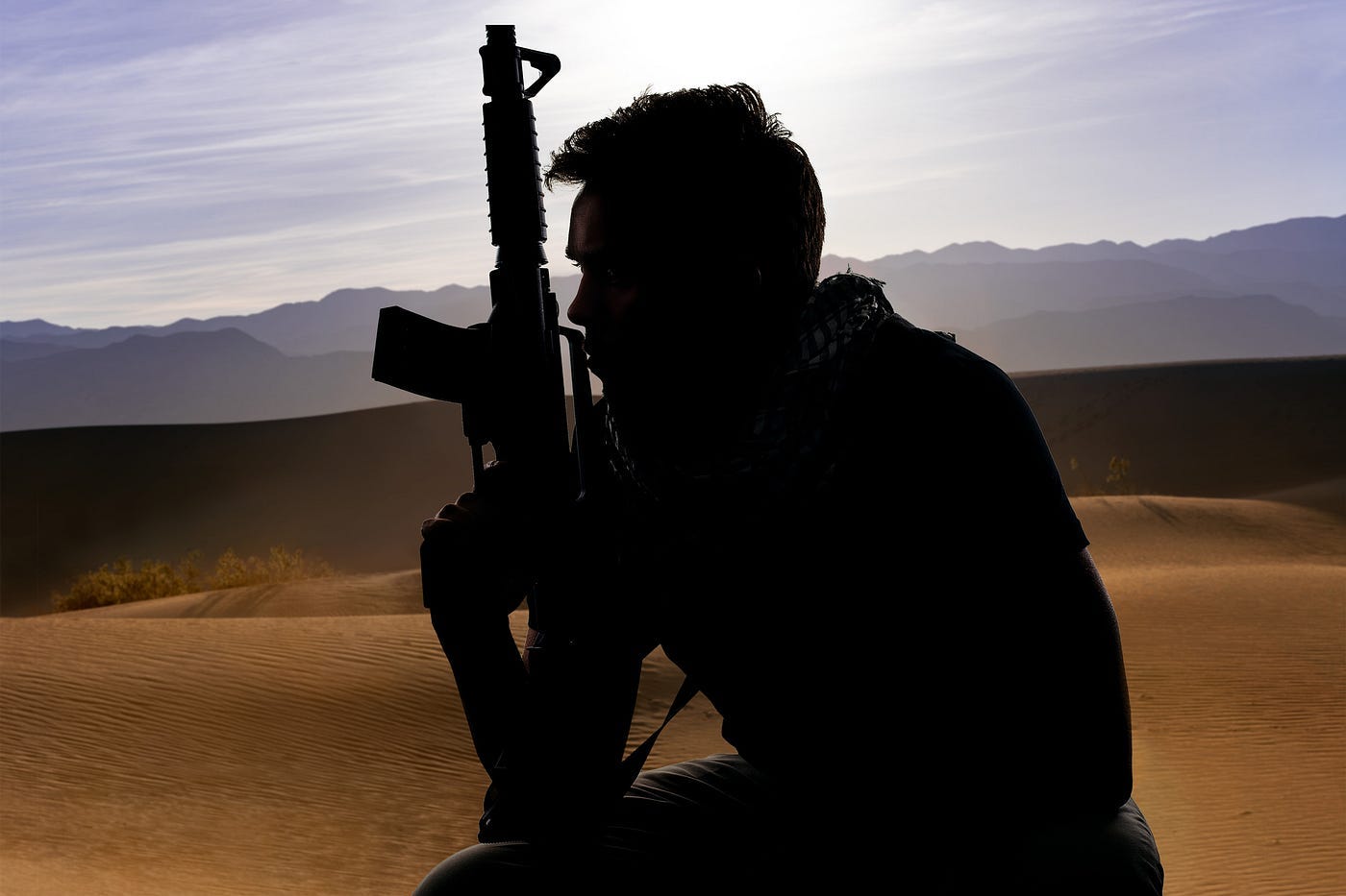 A soldier in the desert, holding his rifle, appears homesick.
