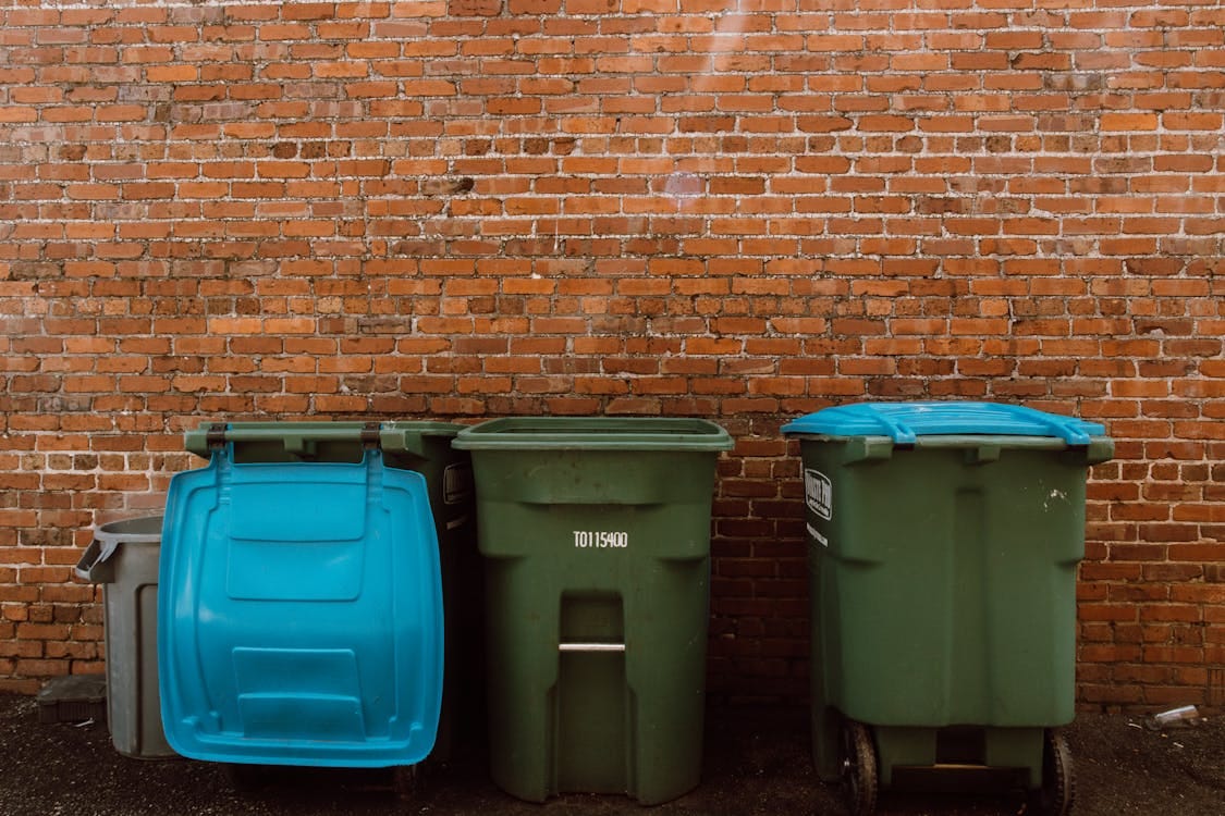 Free Three garbage bins placed in front of a rustic brick wall in an urban setting. Stock Photo
