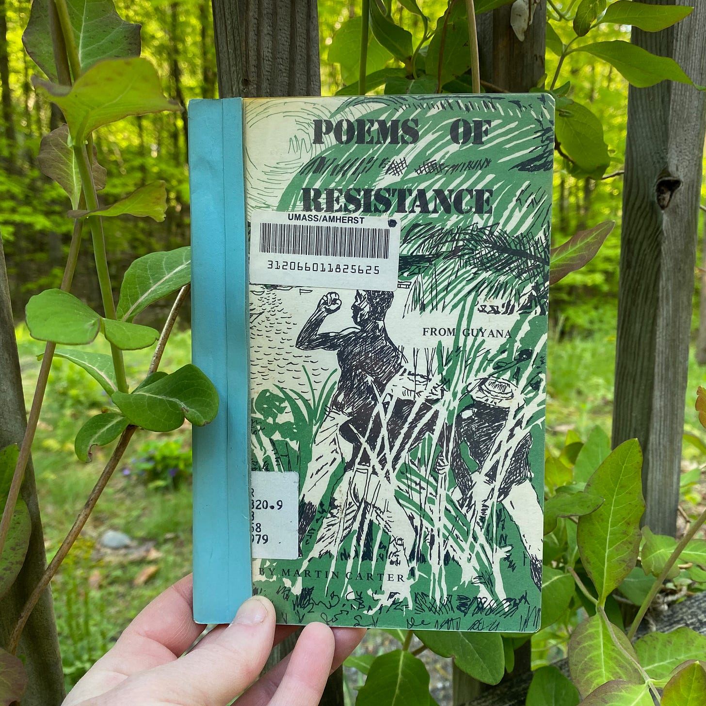 I’m holding Poems of Resistance from Guyana in front of a green vine growing up the side of a porch. 