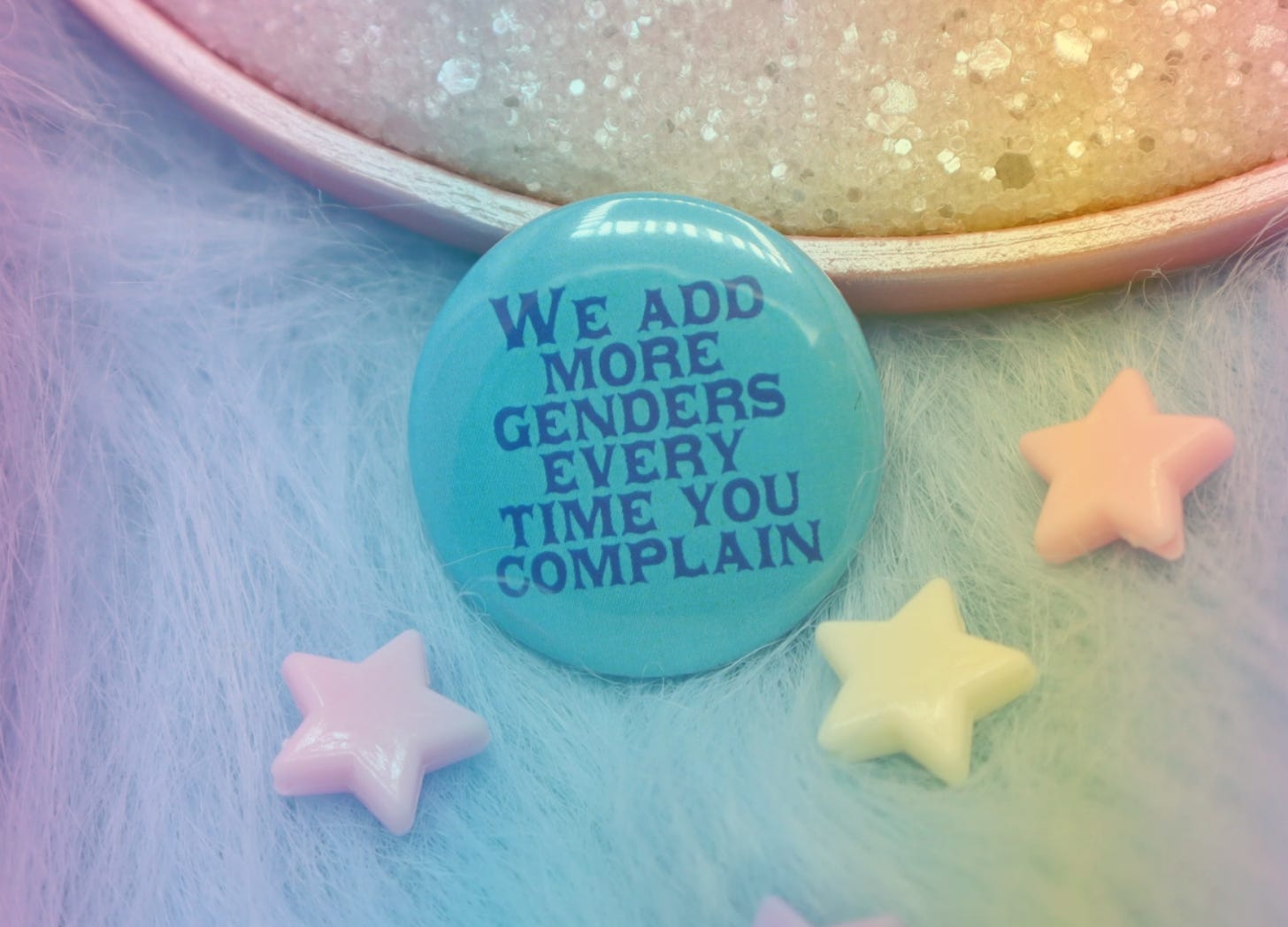 A rainbow-filtered image of a blue button that says "We add more genders every time you complain."