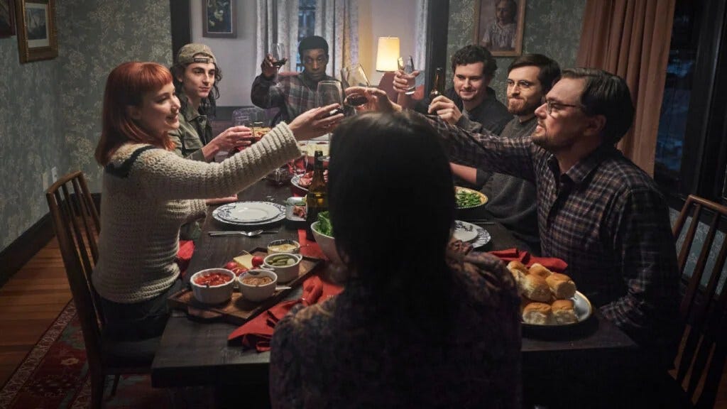 still photograph from a dining scene in the movie "Don't Look Up" with a large group toasting each other at a dining room table.