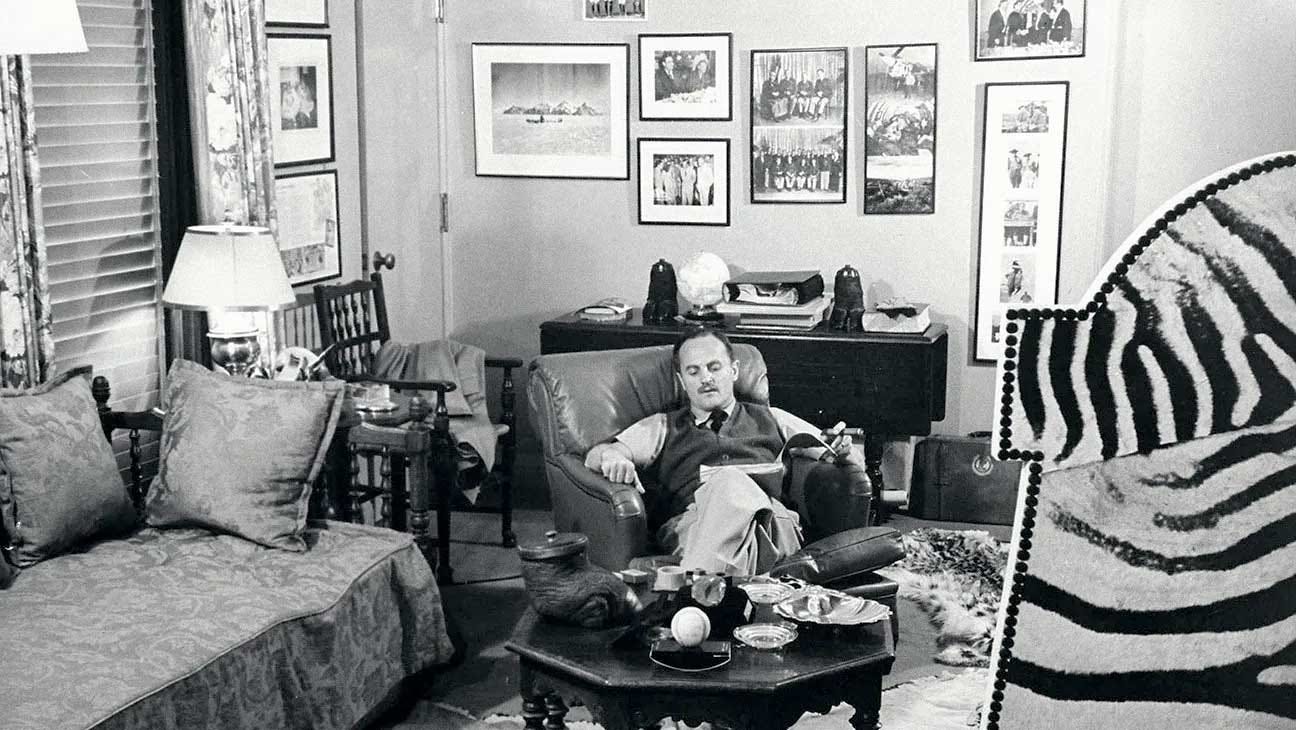 Daryl Zanuck, film producer, in his lounge, reclining in an armchair reading a script and smoking a cigar