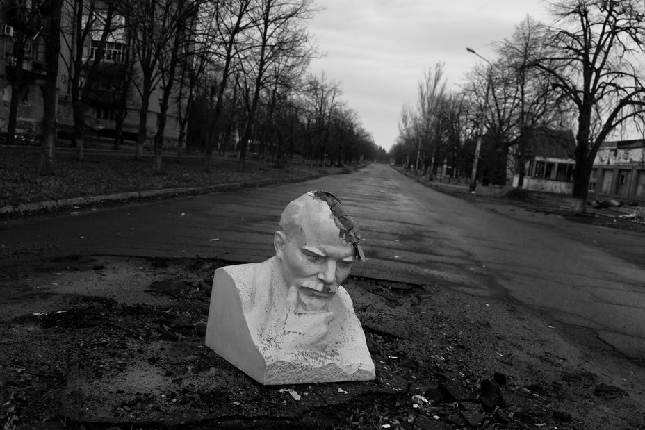black-and-white photo of large sculptural bust in middle of road with part of head destroyed