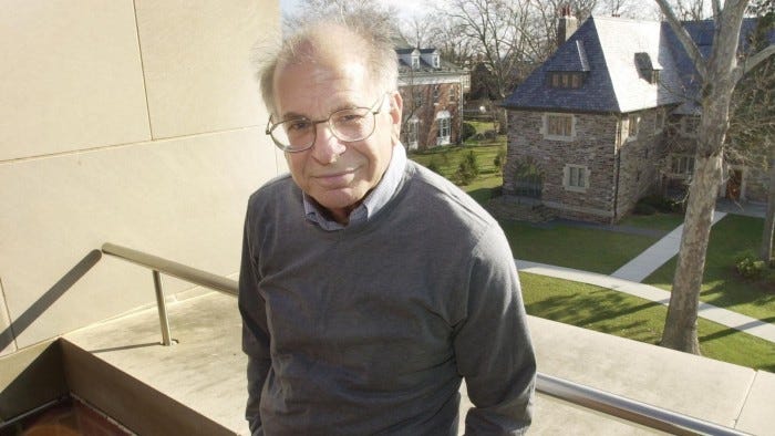 Picture of Daniel Kahneman in glasses, coloured shirt and sweater standing on the balcony of a building at Princeton University