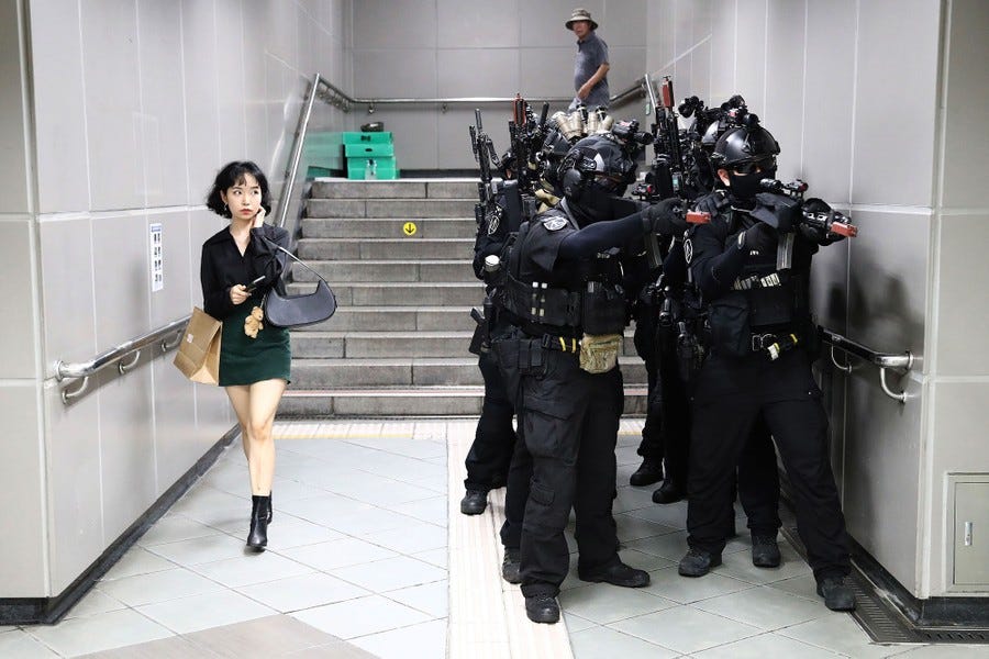 A woman walks past a squad of police officers in heavy gear during an emergency exercise in a subway hall.