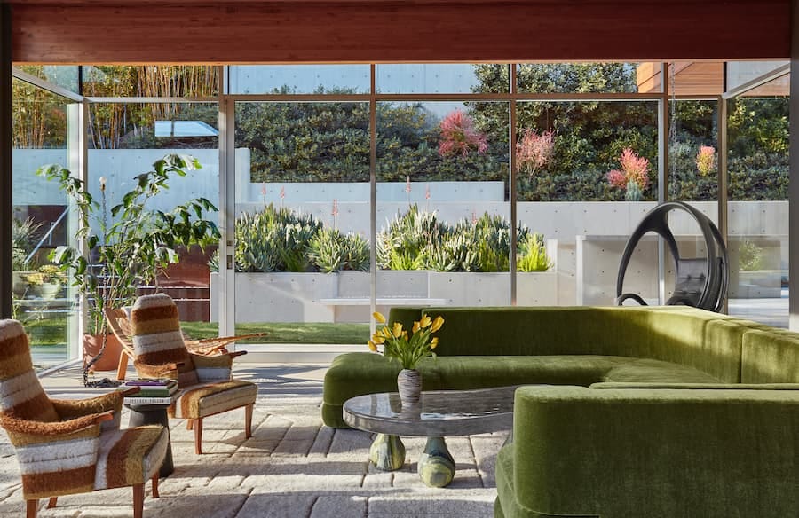 glass room with green sofa and brown chairs linking the outside of nature with the inside