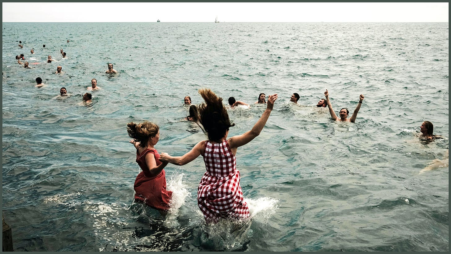 many girls, boys and adults running into and playing in the ocean