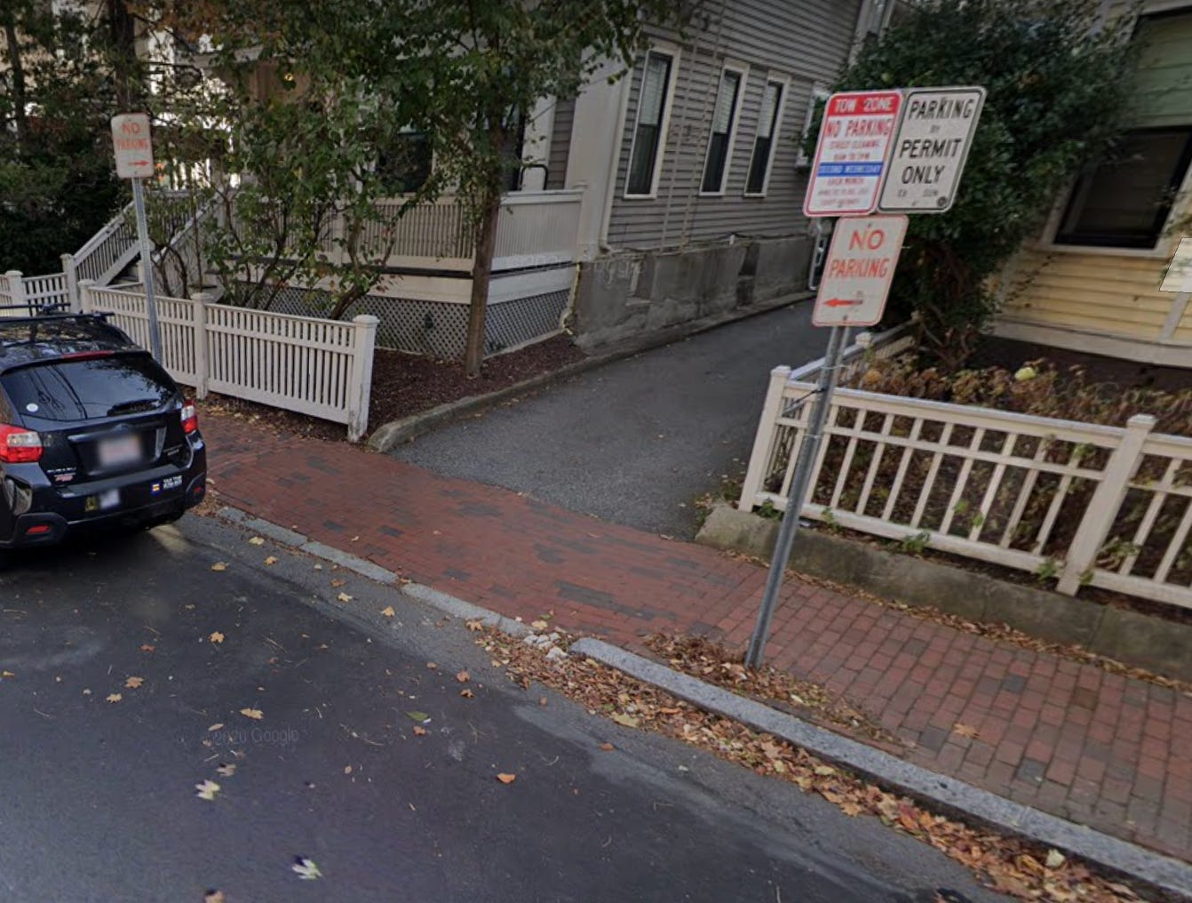 A brick sidewalk and black road. A white fence is on the right. 