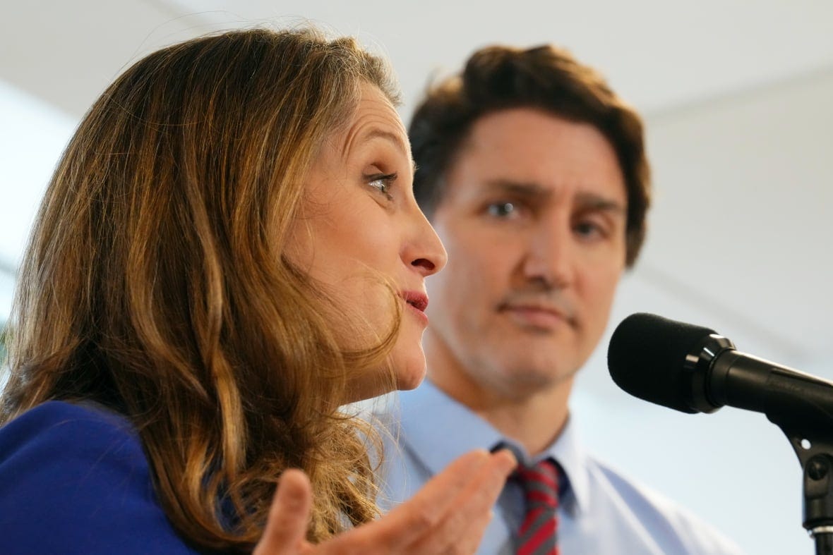 A woman with blonde hair speaks into a microphone while a man with brown hair looks at her