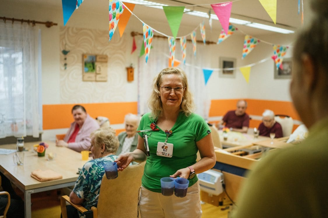 Free A caregiver serving drinks to elderly residents in a cheerful nursing home setting. Stock Photo