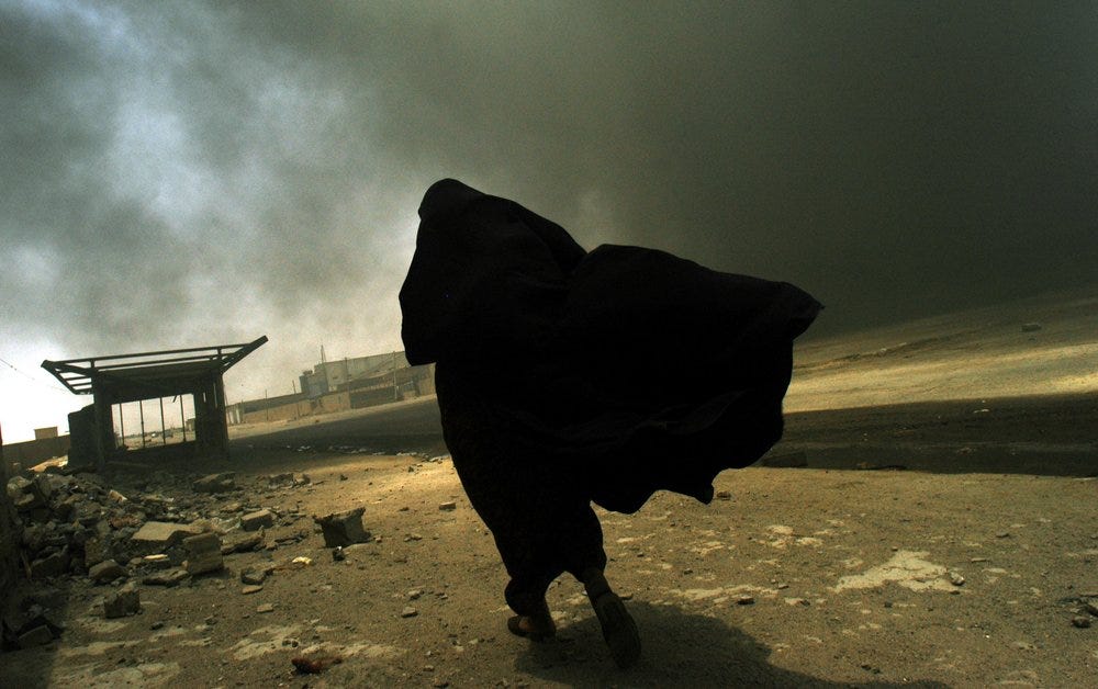 An Iraqi woman walks through smoke rising from a massive fire at a liquid gas factory as she searches for her husband. © Lynsey Addario