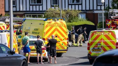 PA Media Locals look on as ambulance and police block the street 