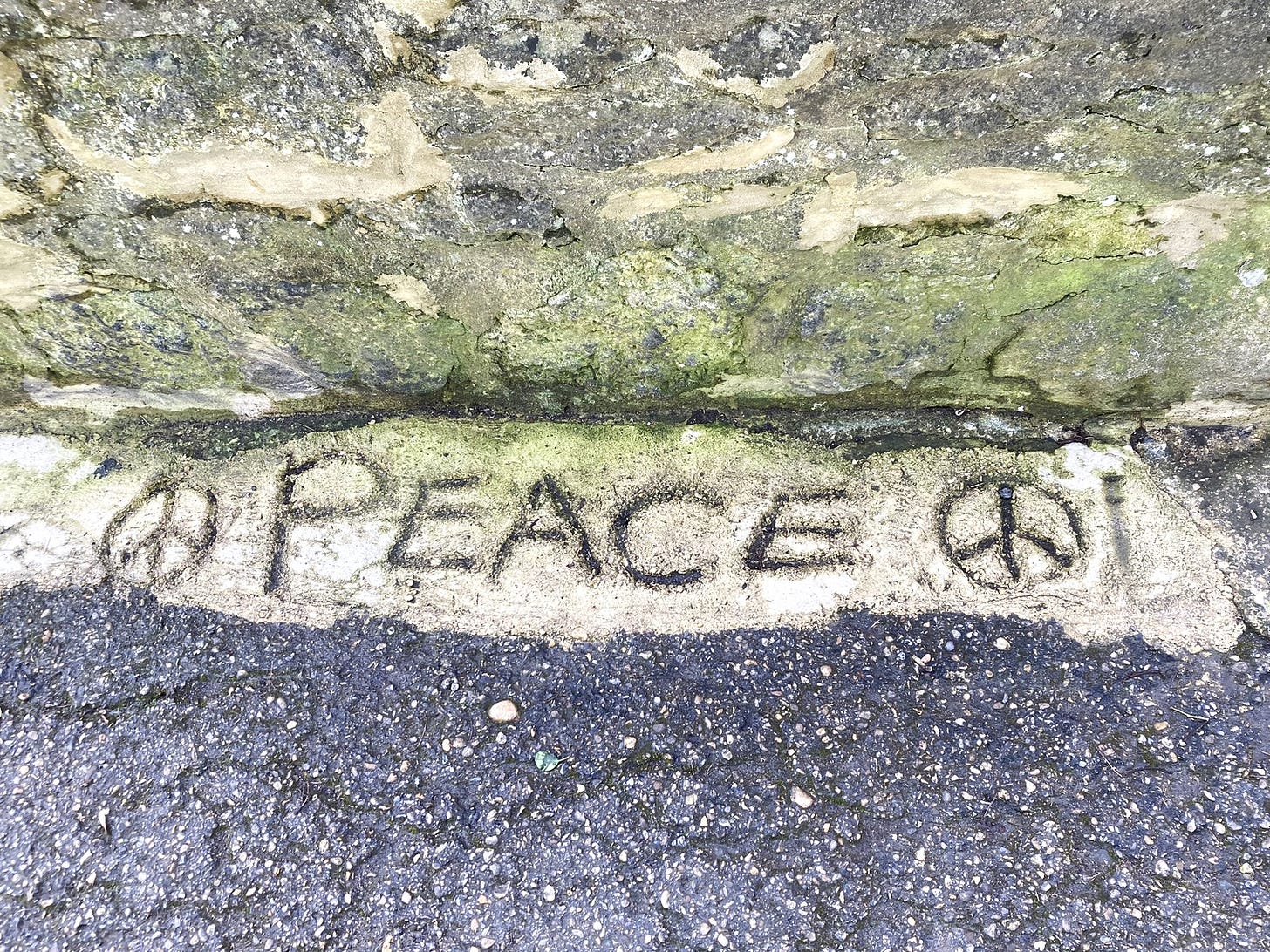 Someone has tried to repair a hole in tarmac with concrete. In the concrete they have written PEACE, in-between two peace signs.