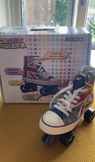 A pair of roller boots. They look like Converse high-tops, patterned in a Union Jack flag, with dark blue wheels. The box is in the background.