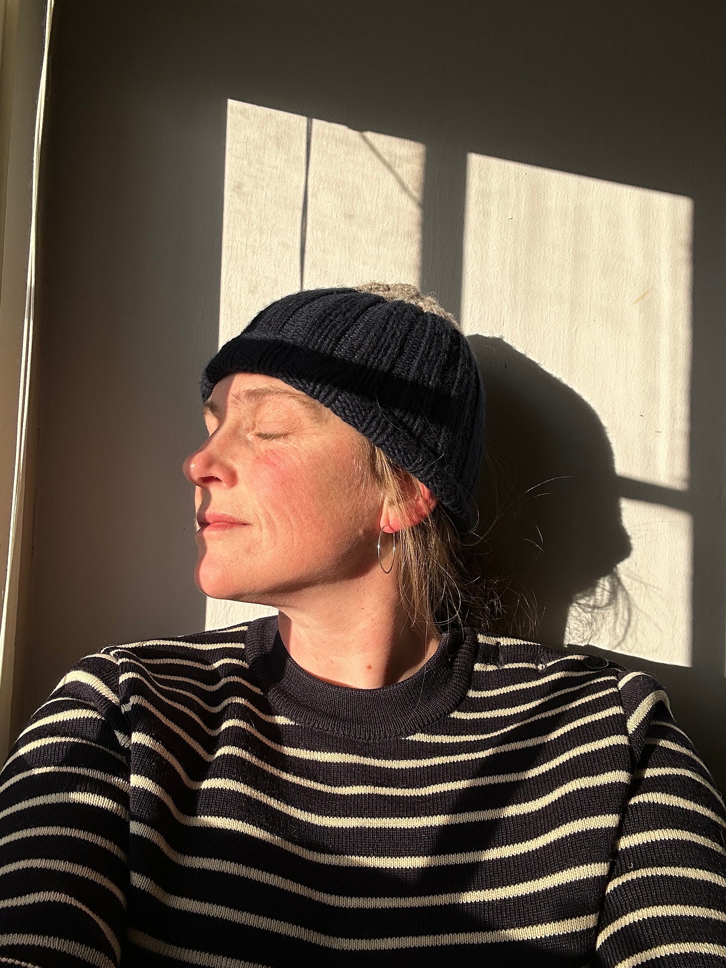 A photo of the artist sitting in sunlight near a window, with her eyes closed