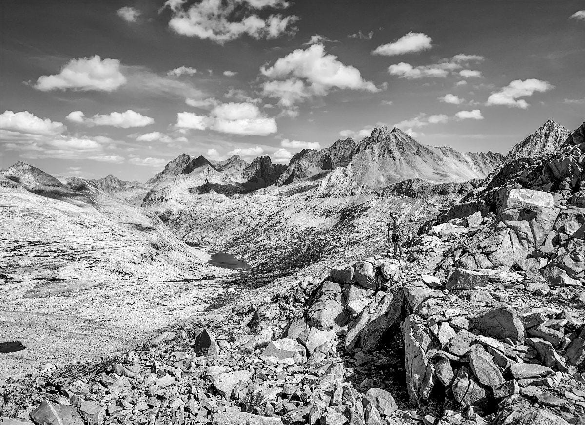 Black and white photo of Scott setting up his tripod on a rocky high mountain pass.