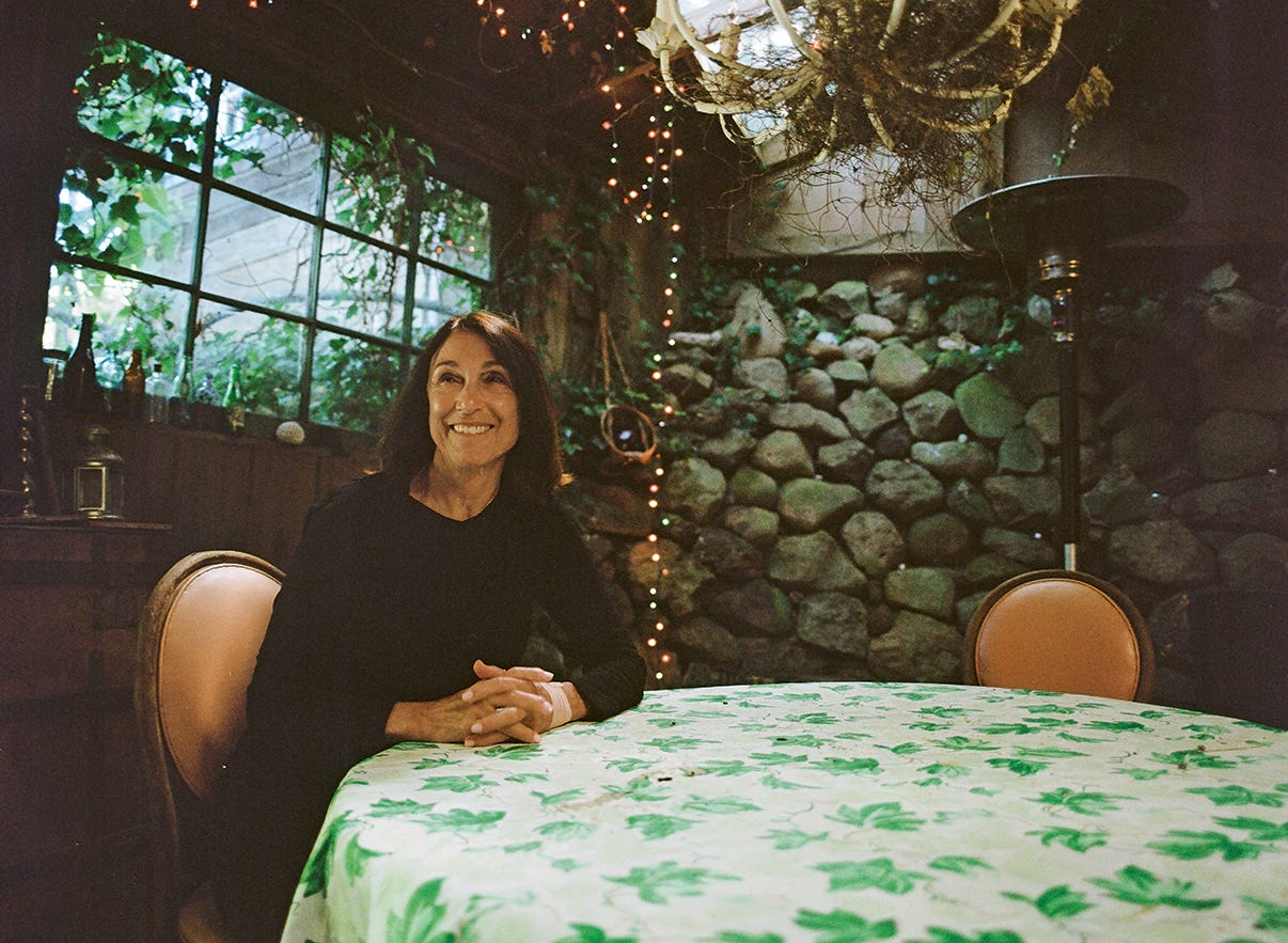 Suzanne Ciani sits at a table with a floral tablecloth in an outdoor dining grotto.