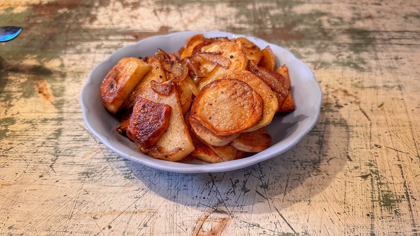 A dish containing the author's attempt at Lyonnaise potatoes. Browned slices of potato and onion are piled up. 