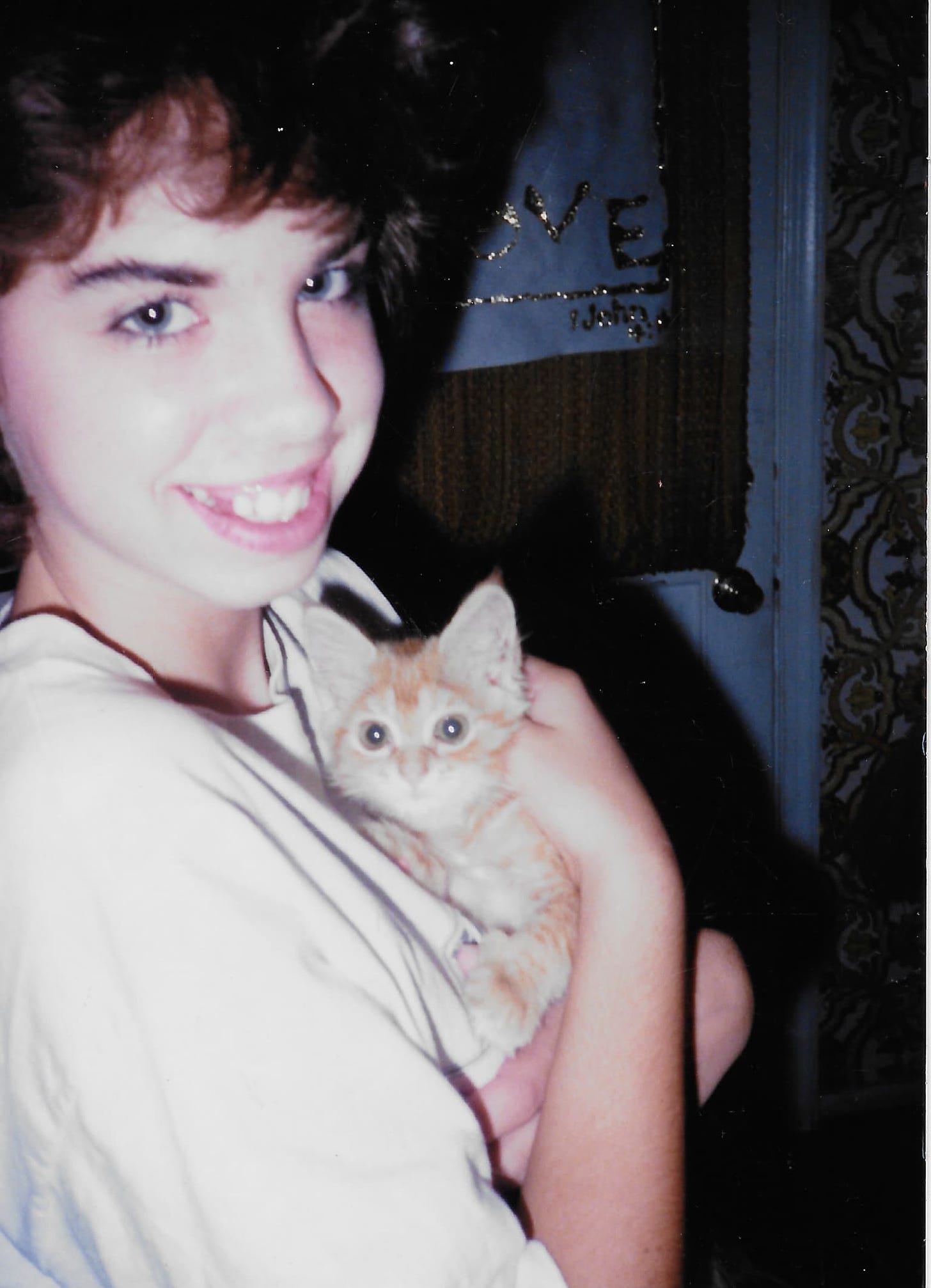A little girl with short brown hair sometime in the 1980's holding a tiny calico kitten, the runt of the litter.