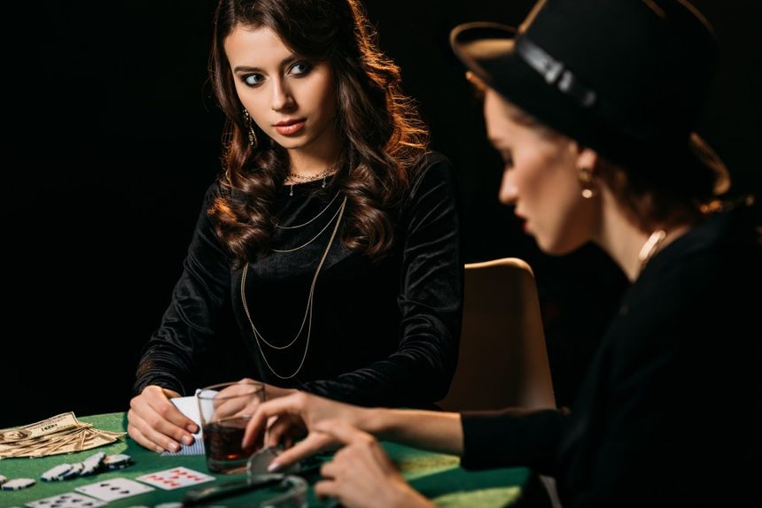 Dark psychology can be used everywhere: Two women playing poker at table in dark room in casino