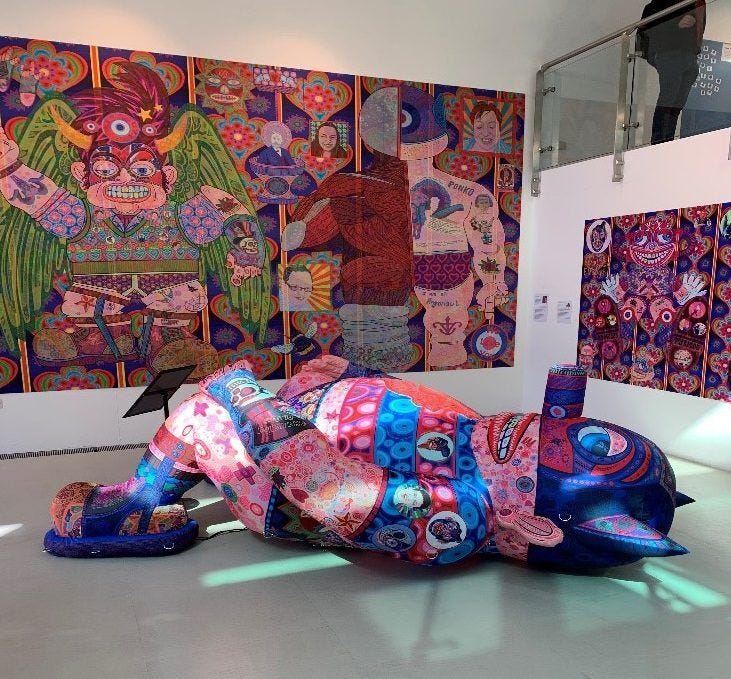 An inflatable sculpture is a figure lying on its back in a gallery. The surface of the sculpture is richly decorated with text and vibrant ‘tattoos’ which tell peoples’ stories from the Changing Places Movement. The motifs on this artwork also give personal reflections about the care that Jason’s mum gave him when he became disabled as a teenager.