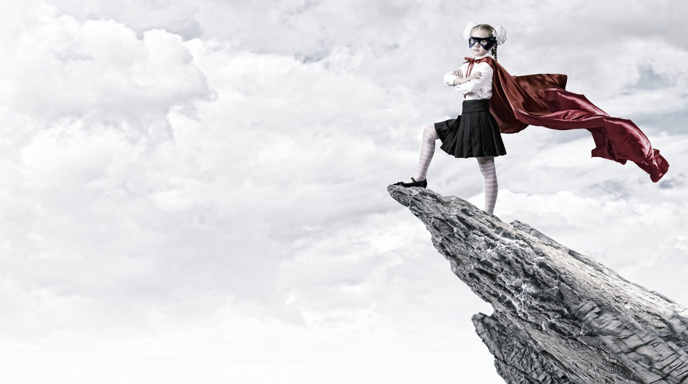 Young girl on a mountain edge wearing a superhero cape