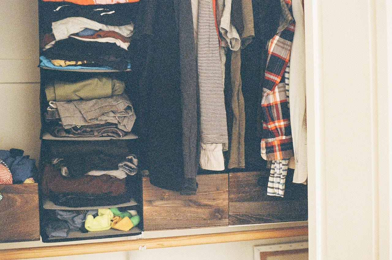 Foto de um closet, com várias roupas empilhadas em prateleiras, tênis na parte de baixo no lado esquerdo, e camisas e casacos alinhados no lado direito.