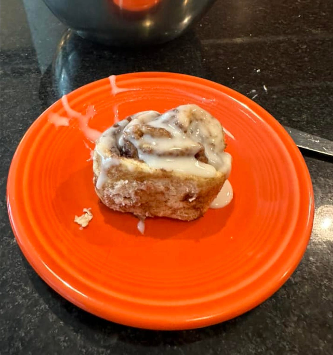an orange plate with a cinnamon roll on top