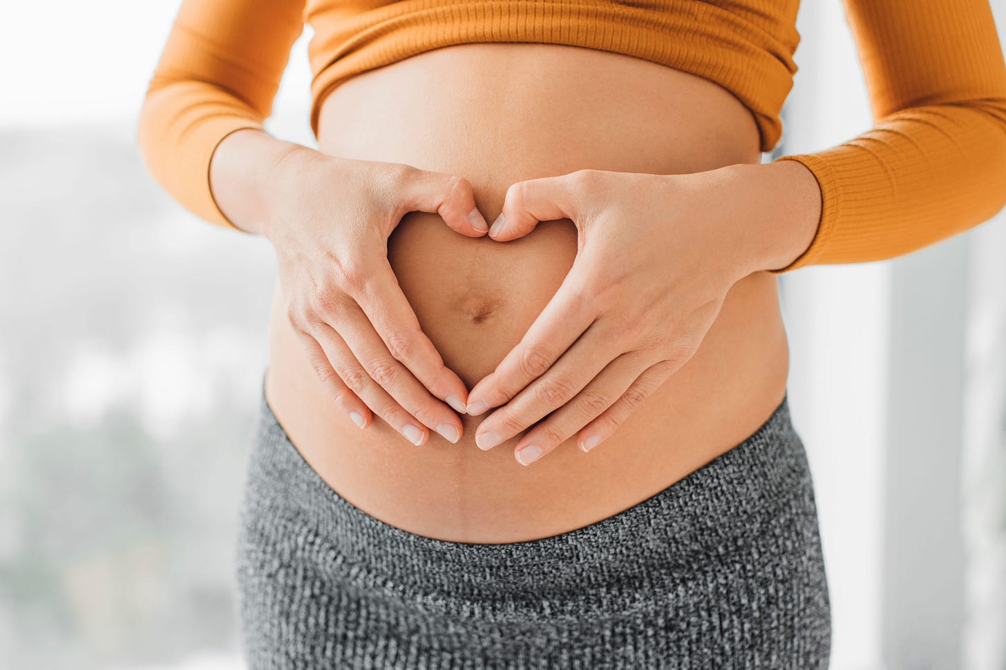 Close up picture of pregnant woman holding stomach in heart shape gesture with hands on her belly