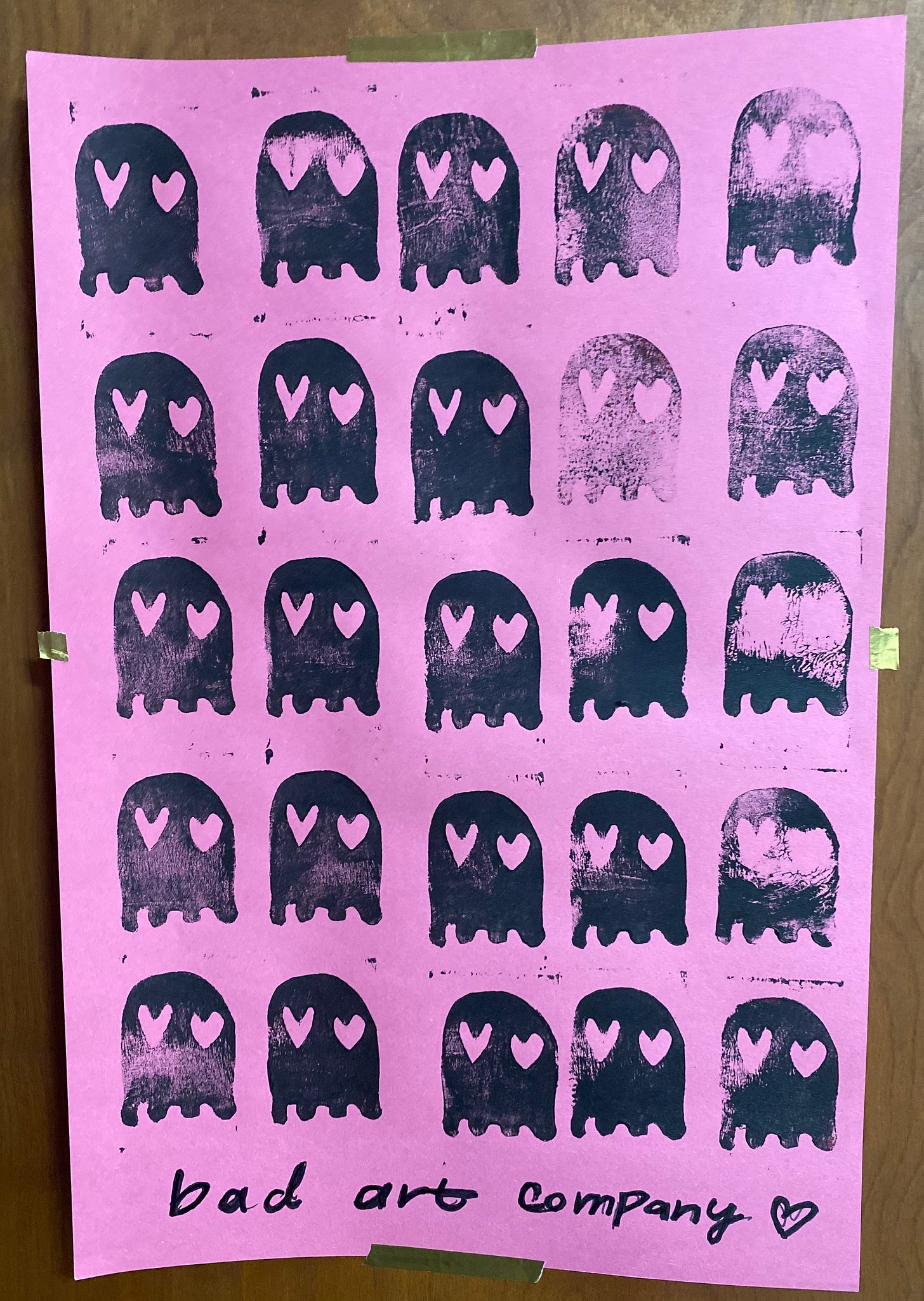 A pink poster with black stamped ghosts with heart eyes on it in a grid pattern.