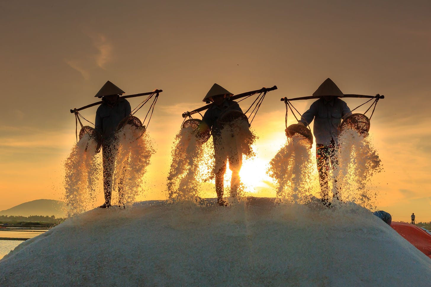 Photo of three men carrying salt at sunset by Quang Nguyen Vinh from Pexels
