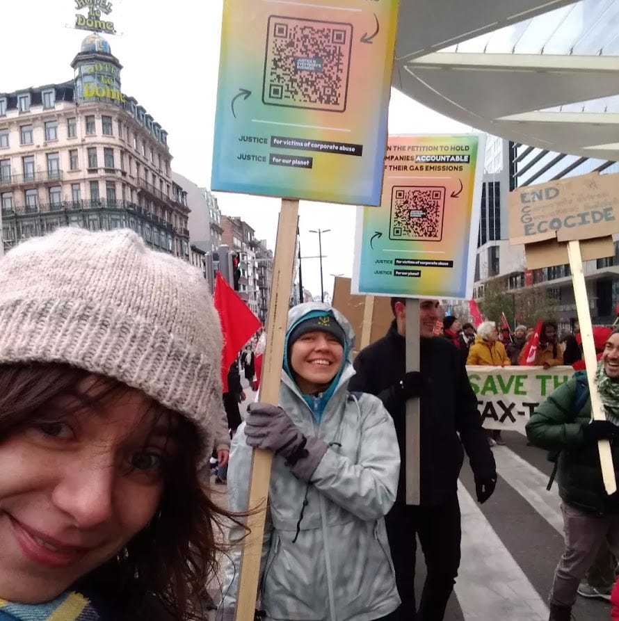 Campaigners in the streets of Brussels holding banners saying 'Sign the petition to hold business accountable' and smiling at the camera